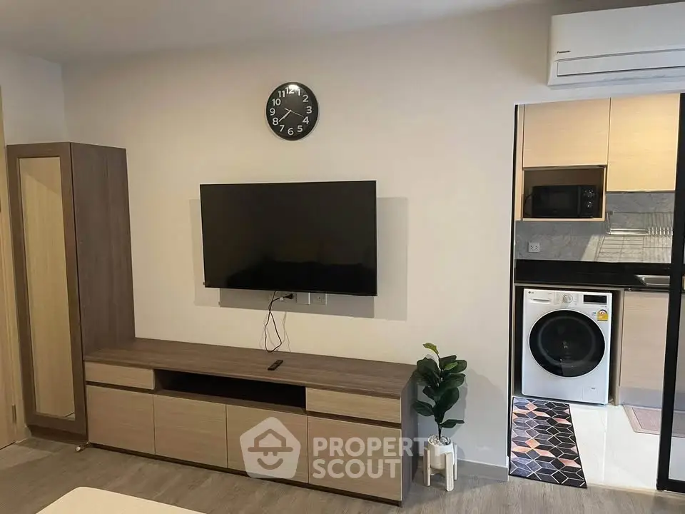 Modern living room with wall-mounted TV and adjacent kitchen featuring washing machine.