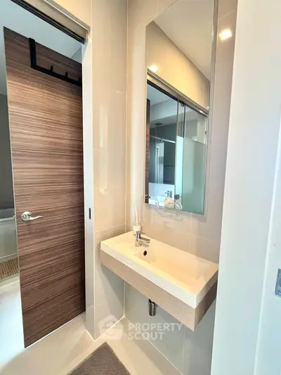 Modern bathroom with sleek sink and wooden door, featuring contemporary design.