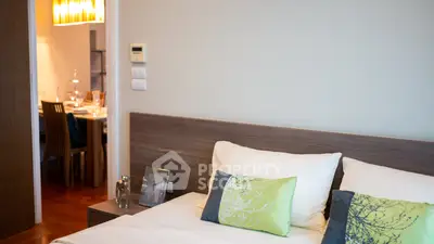 Modern bedroom with elegant decor and view into dining area, featuring stylish pillows and wooden accents.