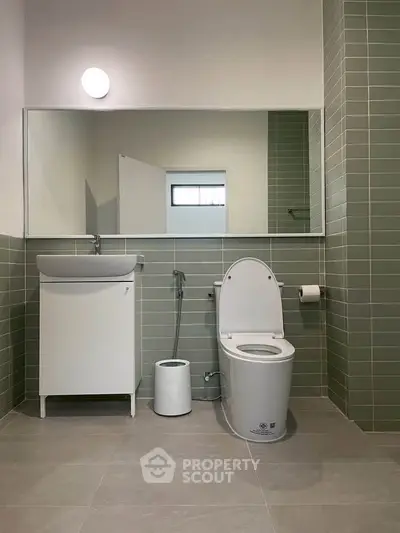 Modern bathroom with sleek design, featuring a toilet, sink, and stylish green tiles.