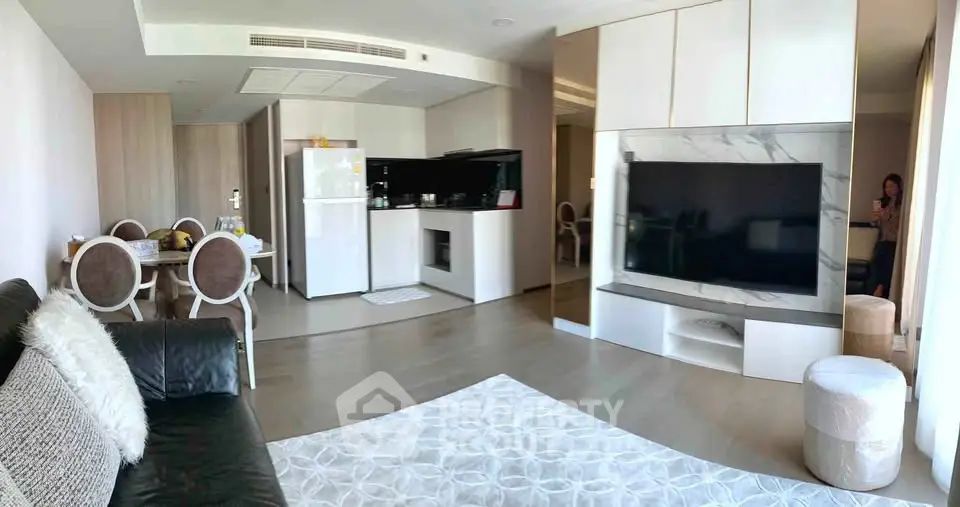 Spacious modern living room with open kitchen and elegant dining area, featuring a large TV and stylish decor.
