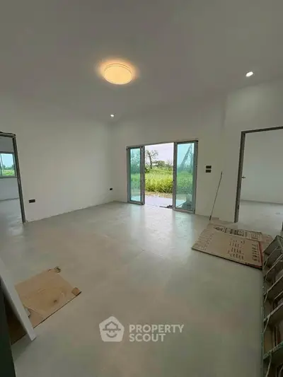 Spacious unfurnished living room with large sliding glass doors opening to a lush green view.