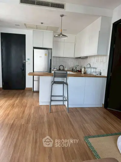 Modern kitchen with sleek white cabinets and wooden flooring, featuring a breakfast bar and stainless steel appliances.