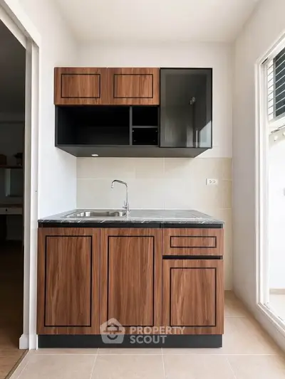 Modern kitchen with sleek wooden cabinets and stainless steel sink in a bright, minimalist space.