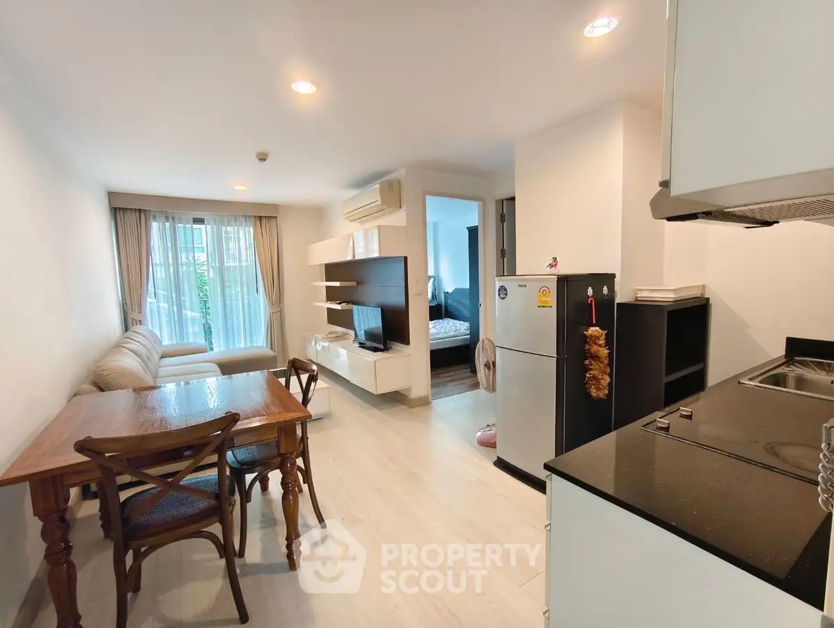 Modern open-layout living room with kitchen and dining area, featuring sleek furniture and natural light.
