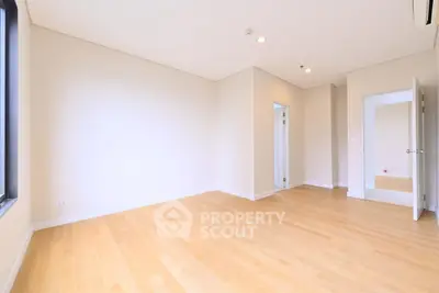 Spacious empty bedroom with wooden flooring and natural light, perfect for customization.
