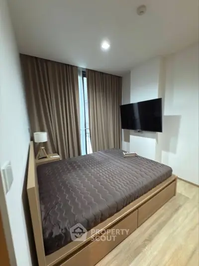 Modern bedroom with large bed, wall-mounted TV, and floor-to-ceiling window with curtains.