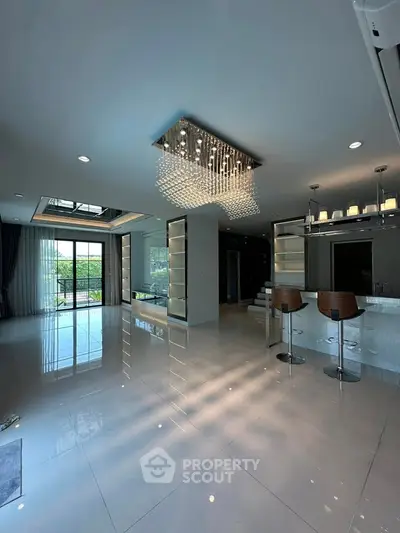 Luxurious open-plan living room with elegant chandelier and modern bar stools.