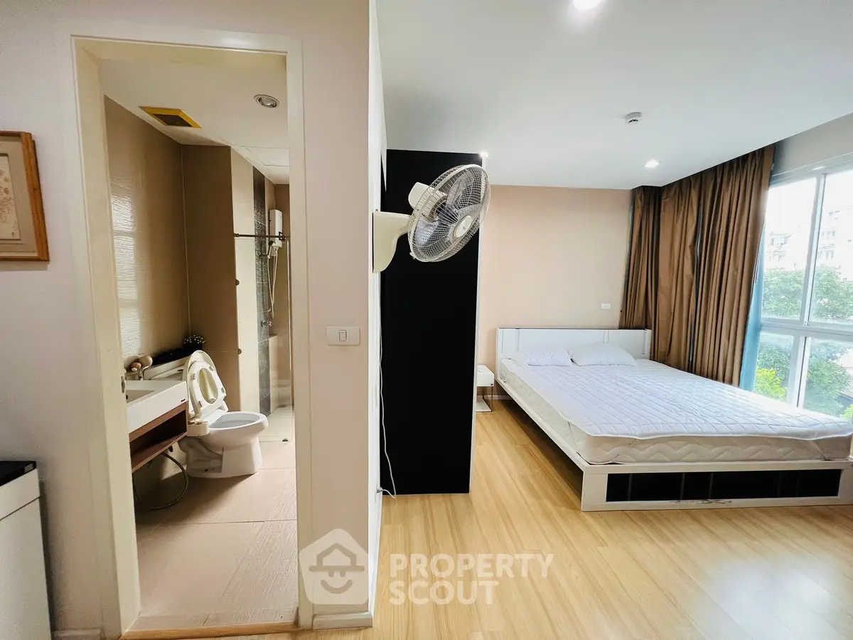 Modern studio apartment with bedroom and bathroom, featuring large window and wooden flooring.