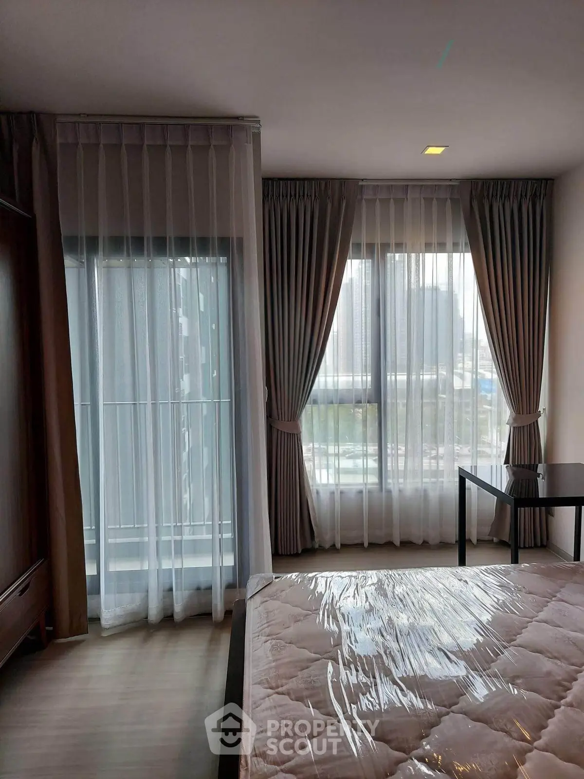 Modern bedroom with large windows and elegant curtains in a high-rise apartment.