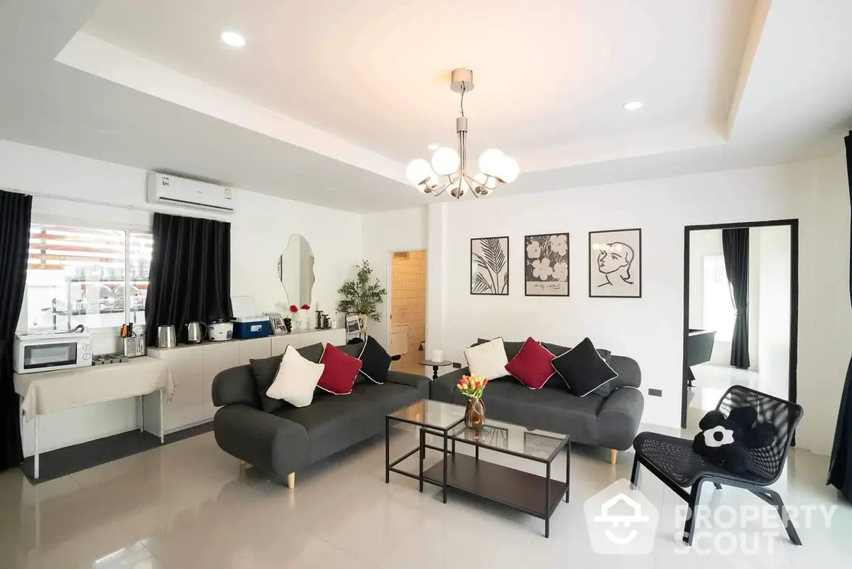 Spacious modern living room with sleek furniture and stylish decor, featuring a comfortable seating area, elegant light fixtures, and a neat kitchen in the background, perfect for entertaining.