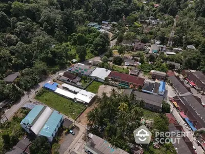 Aerial view of a tropical residential area with lush greenery, showcasing a variety of homes and buildings nestled among the trees, offering a serene and peaceful living environment.