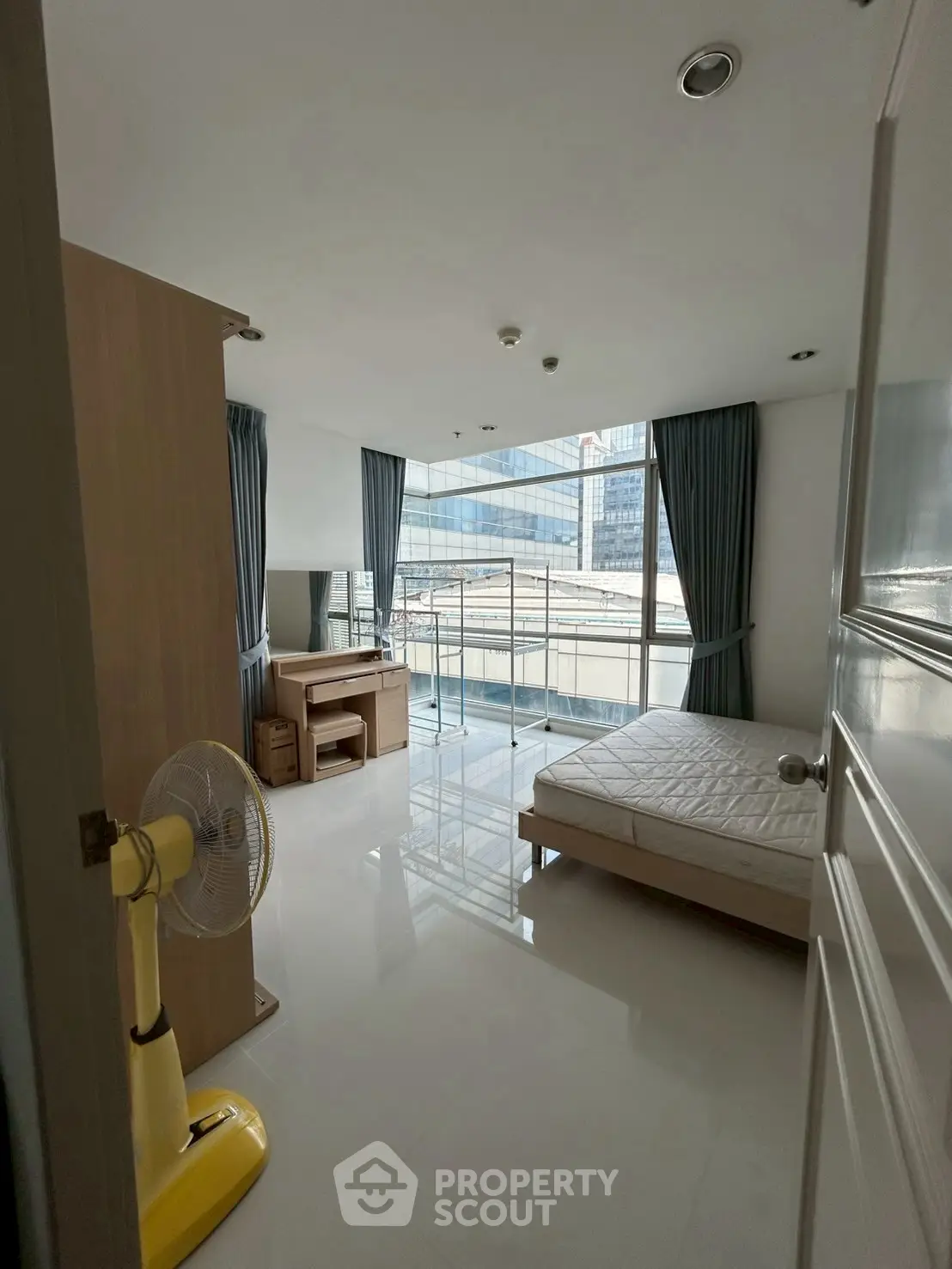 Bright bedroom with large windows and city view, featuring modern furniture and sleek design.