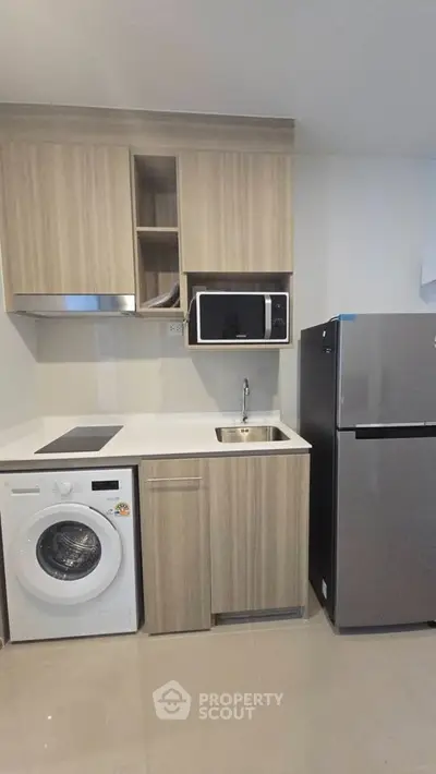 Modern kitchen with sleek appliances, featuring a washing machine, microwave, and fridge in a compact layout.