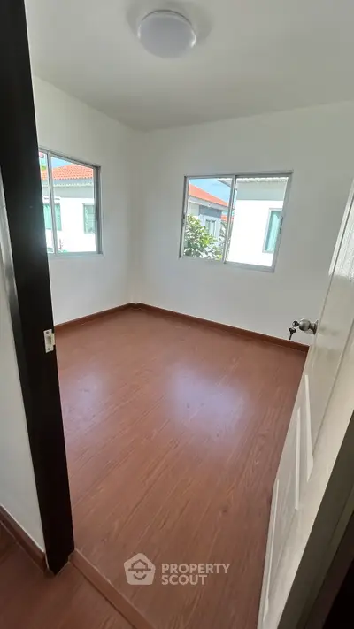 Bright empty room with wooden flooring and two windows, ideal for customization.