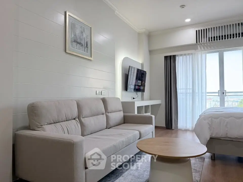 Modern living room with cozy sofa and wall-mounted TV, featuring a bright window view.