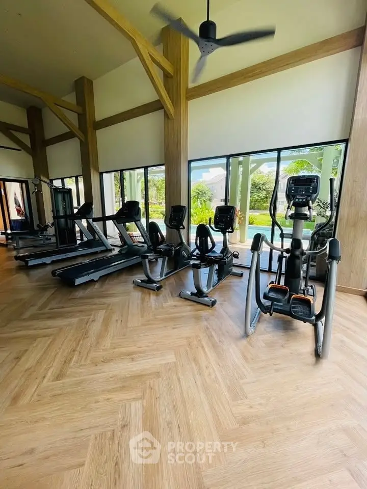Spacious gym with modern equipment and large windows overlooking greenery.