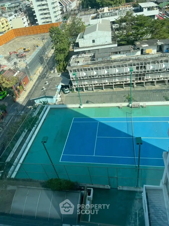 Aerial view of a residential building with a tennis court and urban surroundings.
