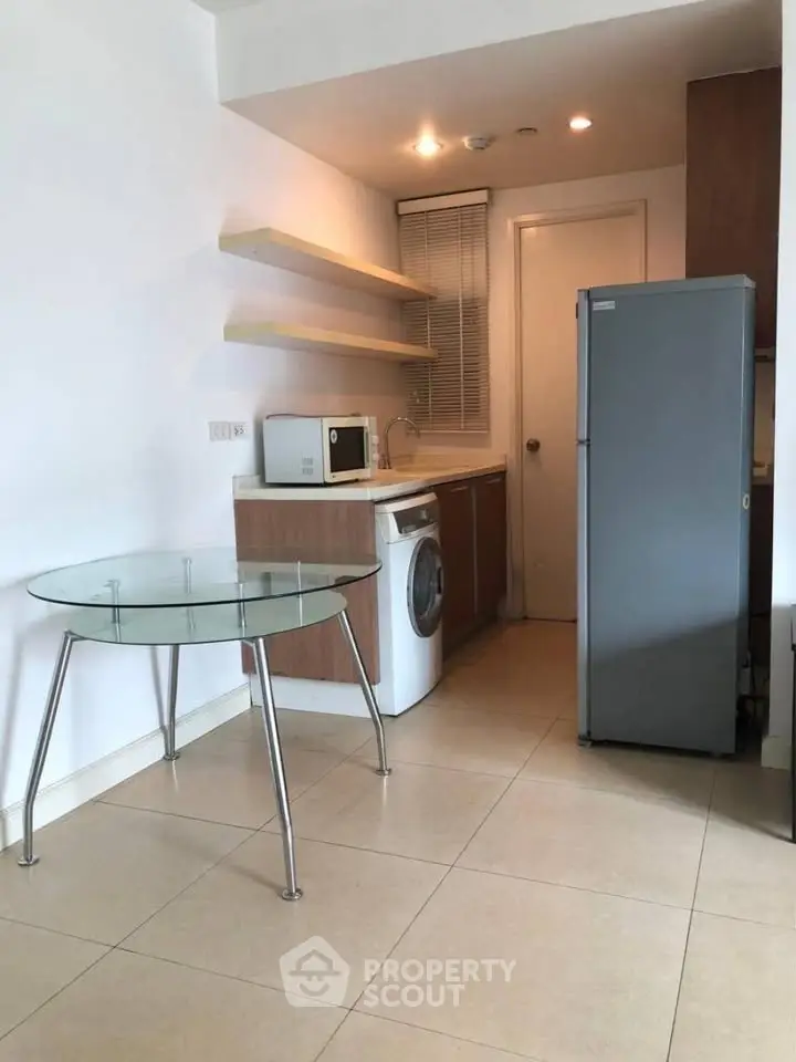 Modern kitchen with glass table, washing machine, and sleek appliances in compact layout.