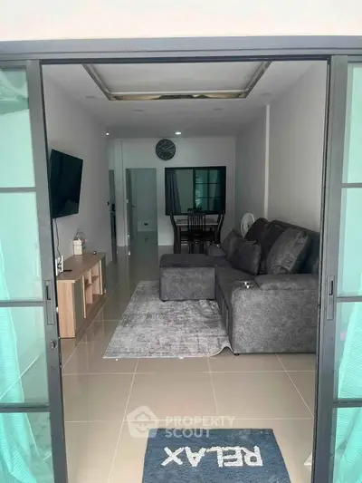 Modern living room with sleek gray sofa and wall-mounted TV, open to dining area.