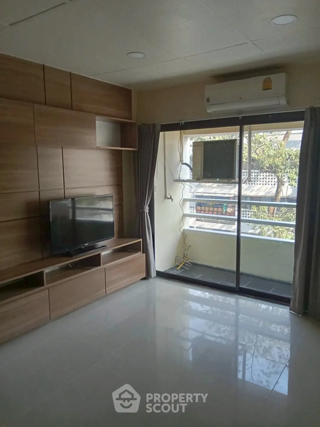 Modern living room with TV and balcony view, featuring sleek wooden paneling and air conditioning.