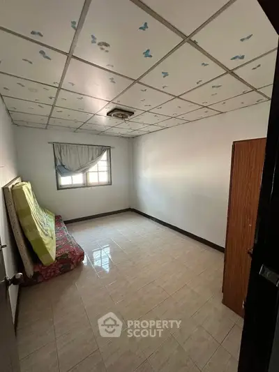 Spacious bedroom with tiled floor and ceiling decor, featuring a window for natural light.