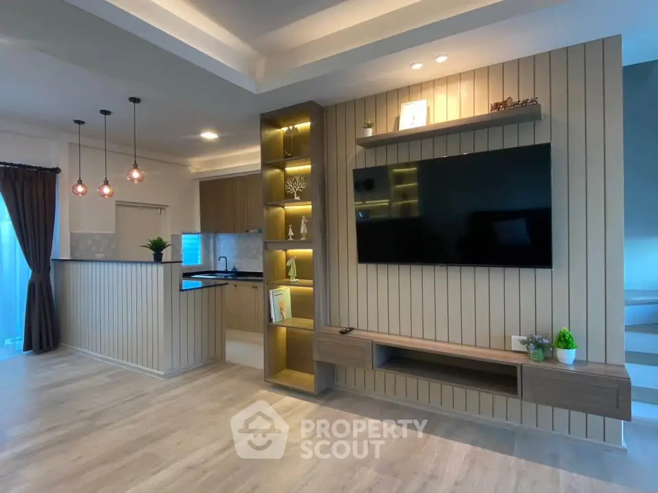 Modern living room with open kitchen, stylish lighting, and built-in TV unit in a contemporary home.