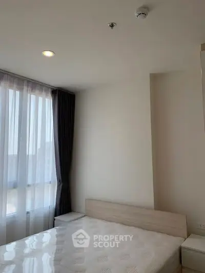 Modern bedroom with large window and natural light, featuring a comfortable bed and elegant curtains.