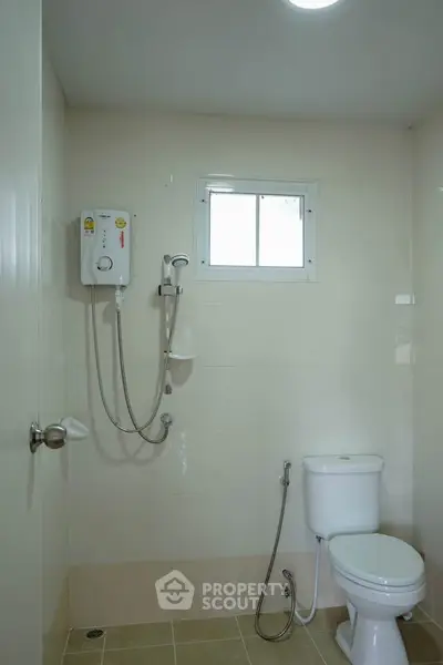 Modern bathroom with shower heater and window, featuring clean tiles and essential fixtures.