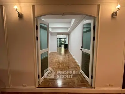 Spacious open living area with elegant wooden flooring and double doors leading to a bright space.