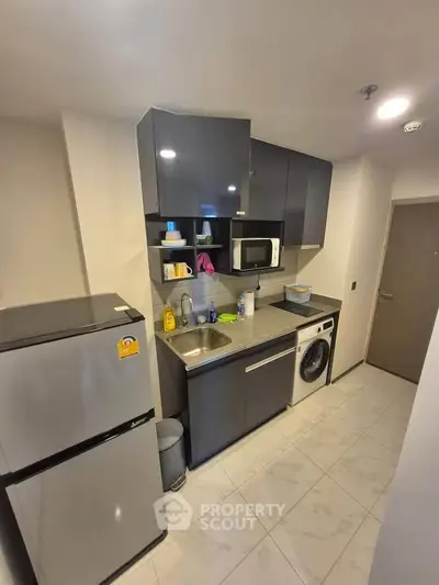 Modern compact kitchen with sleek cabinets, stainless steel appliances, and washing machine in urban apartment.