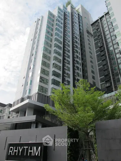 Modern high-rise building with sleek architecture and lush greenery in urban setting.
