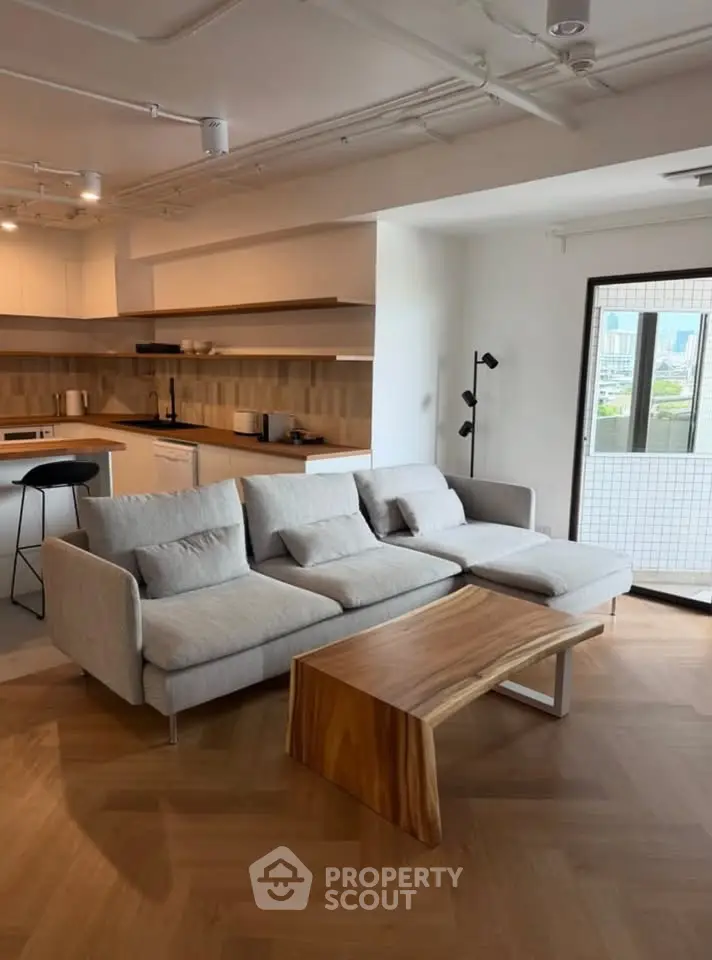 Modern living room with stylish sofa and wooden coffee table, open kitchen layout, and city view balcony.