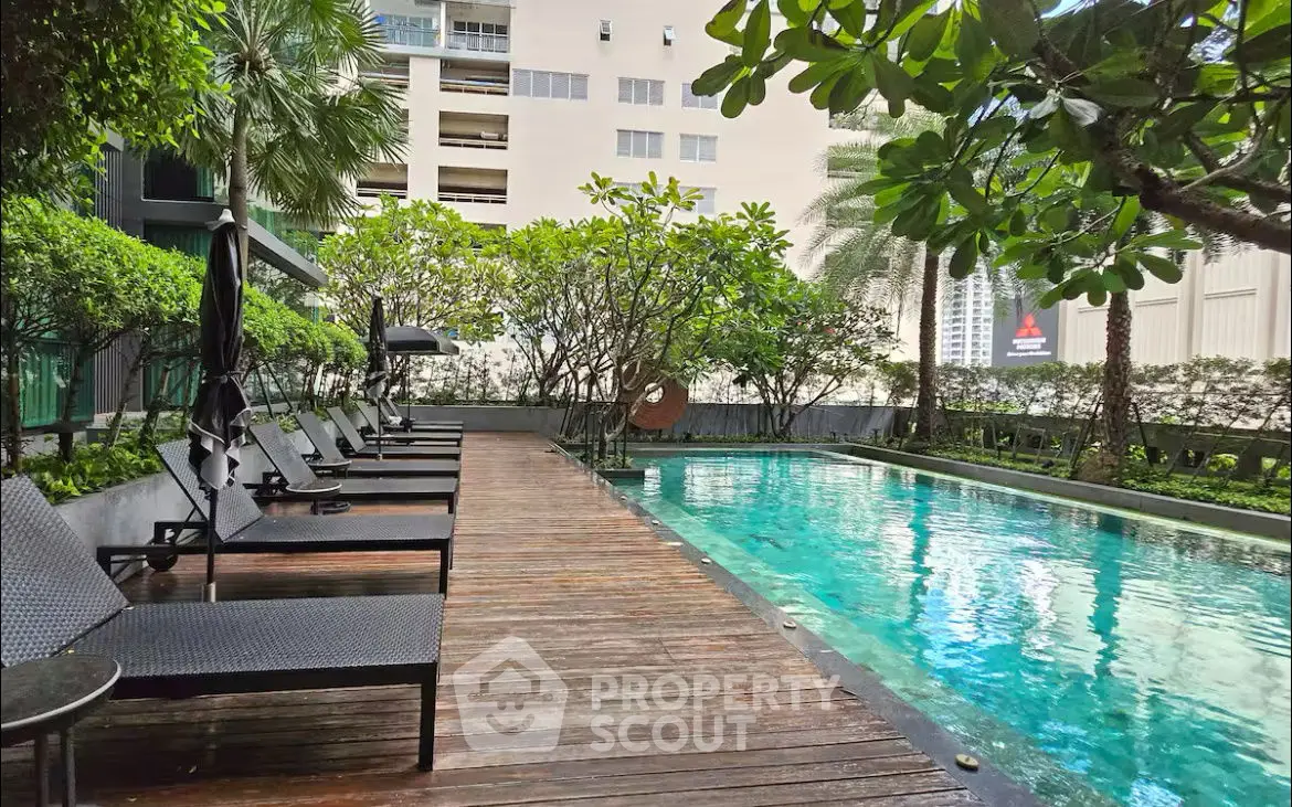 Luxurious outdoor pool area with lush greenery and modern lounge chairs in a high-end residential complex.