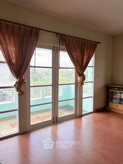 Bright living room with large windows and balcony access, featuring elegant curtains and wooden flooring.