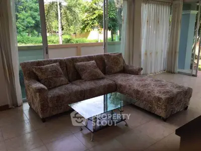 Spacious living room with floral sectional sofa and glass coffee table overlooking lush greenery.