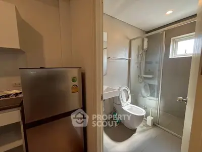 Compact apartment bathroom with modern fixtures and adjacent kitchenette featuring a fridge.