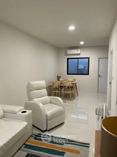 Modern living room with white leather furniture and dining area, featuring sleek design and ample lighting.