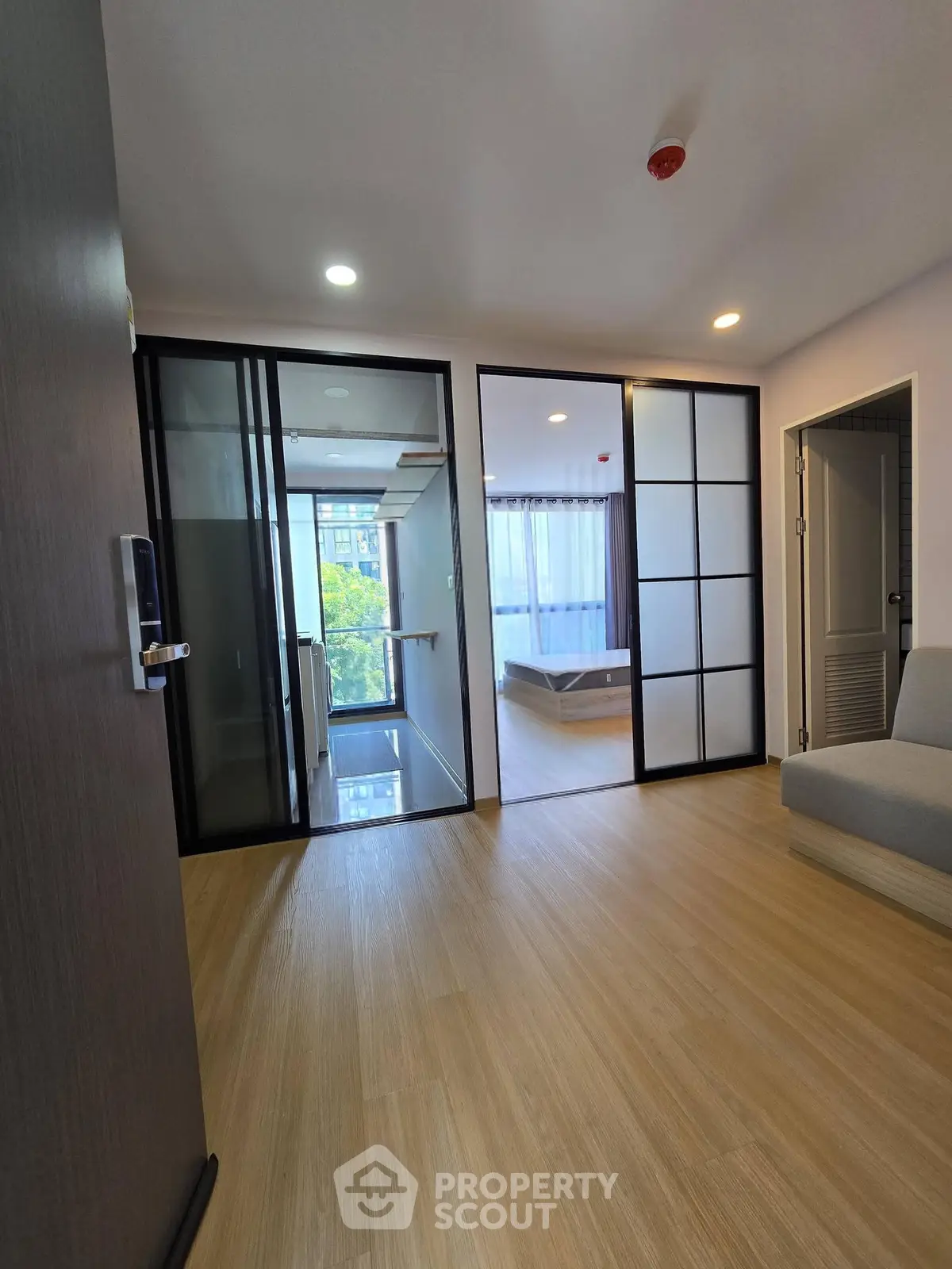 Modern apartment interior with wooden flooring and sliding glass doors leading to a bedroom.
