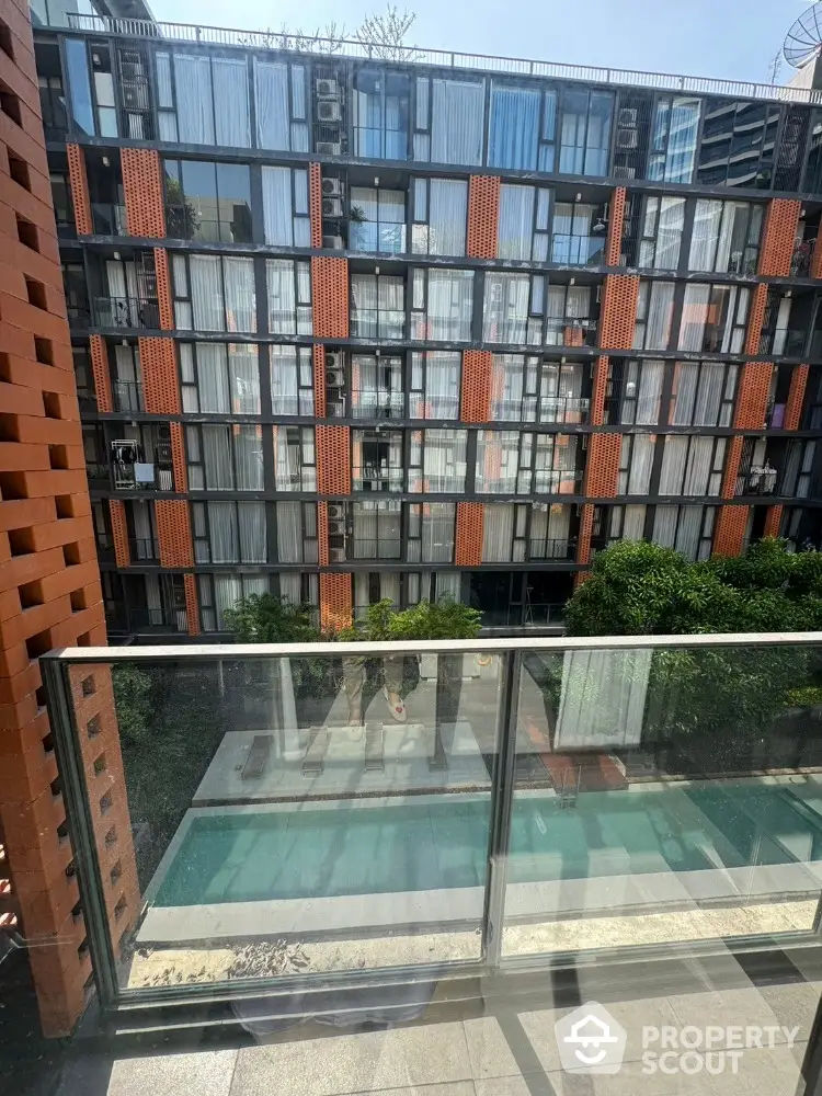 Modern apartment building with pool view from balcony, featuring sleek glass and brick design.