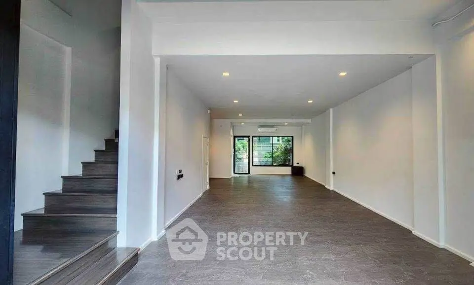 Spacious open-plan living area with modern staircase and large window view.