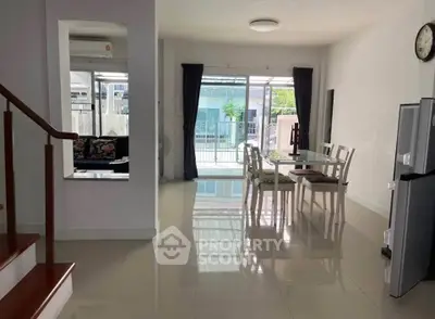 Spacious dining area with glass table and chairs, adjacent to a bright living space with large windows.
