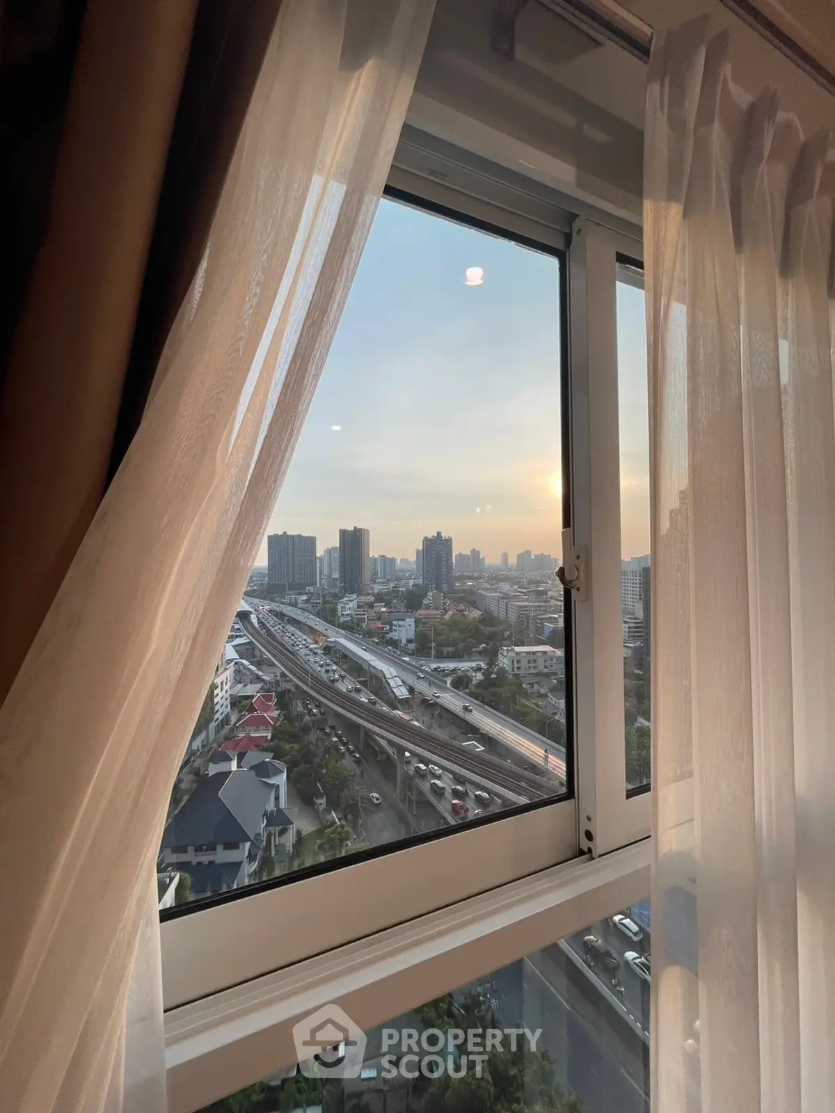 Stunning cityscape view from a high-rise apartment window at sunset, showcasing urban living.