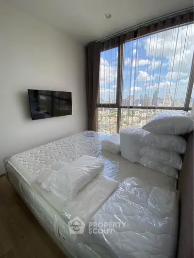 Modern bedroom with city view, featuring a wall-mounted TV and large windows for natural light.