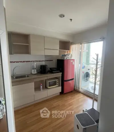 Modern kitchen with red fridge and microwave, bright natural light from balcony, sleek cabinetry.
