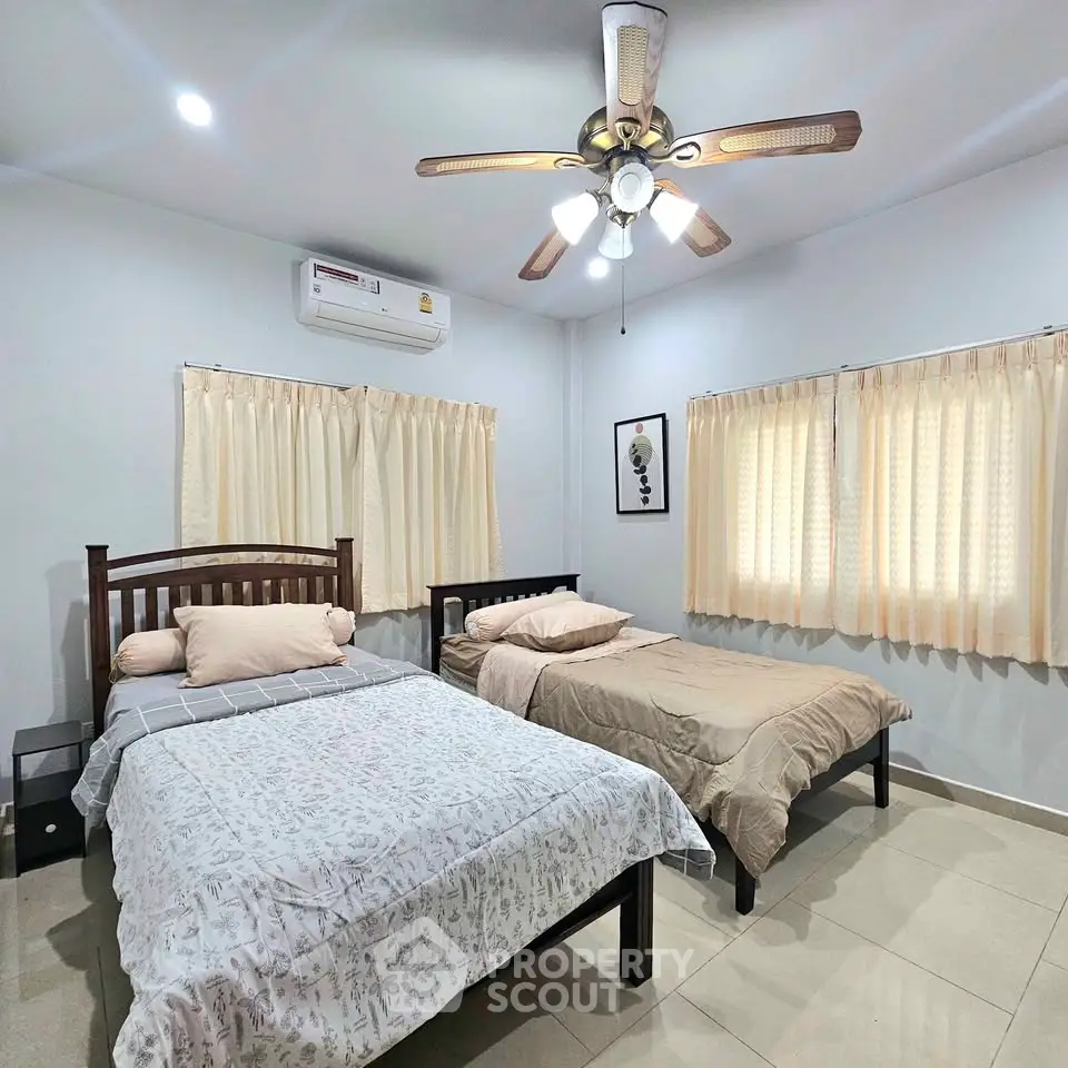 Spacious bedroom with two beds, ceiling fan, and natural light from windows.