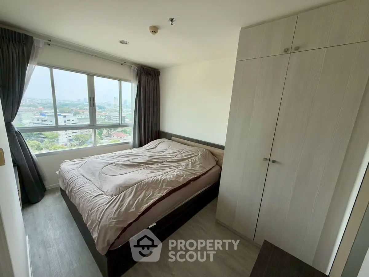 Cozy bedroom with large window offering stunning city views and ample natural light.