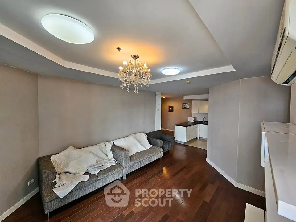 Spacious living room with elegant chandelier and modern kitchen in open layout apartment.