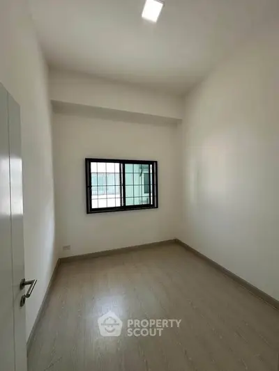 Spacious empty room with large window and wooden flooring, perfect for customization.