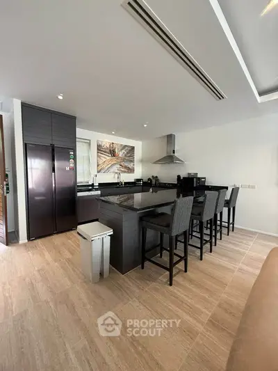 Modern kitchen with sleek black countertops and high chairs, featuring stainless steel appliances and elegant decor.